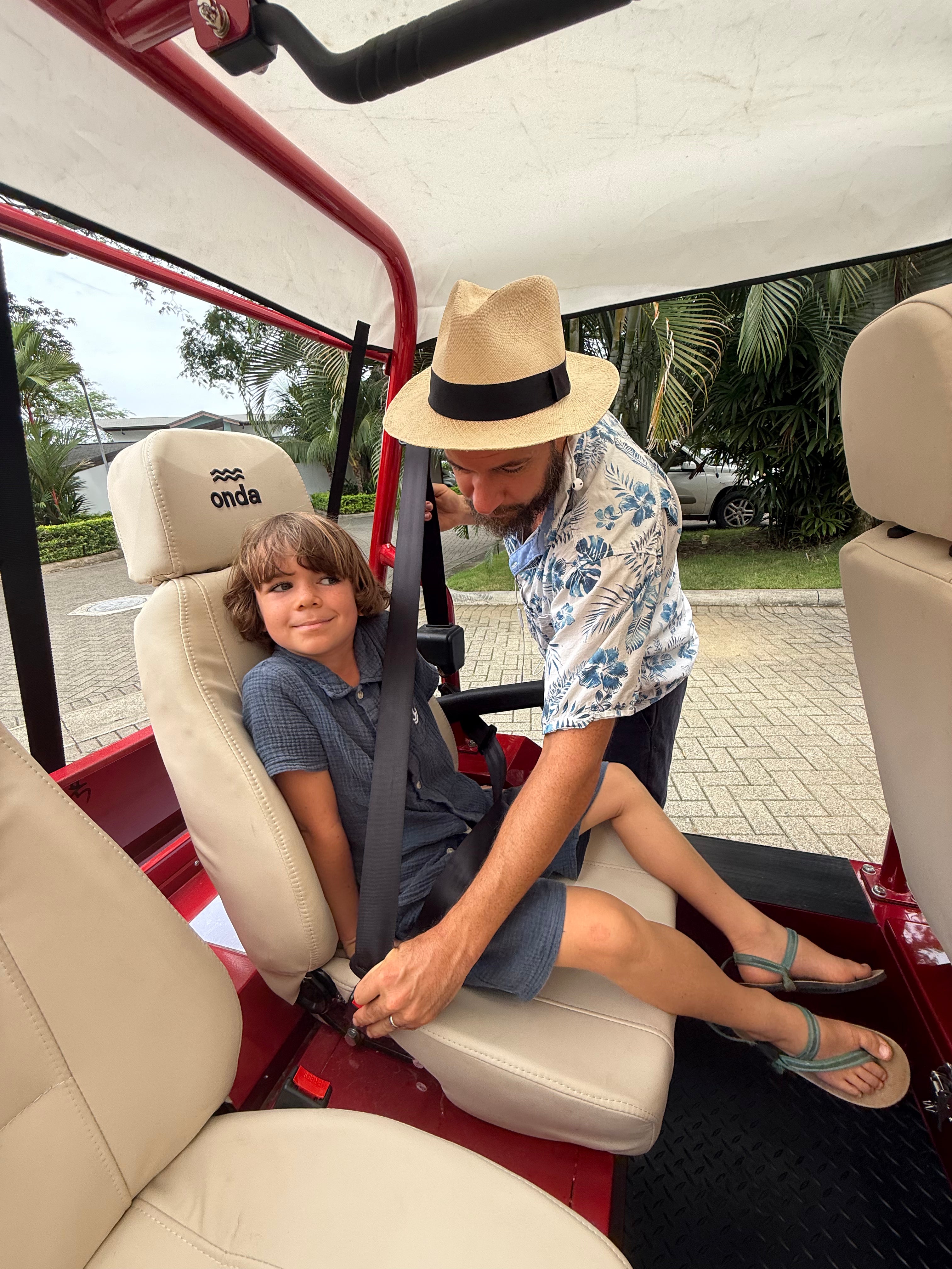 Man buckling a child in a golf cart with 'onda' branding.