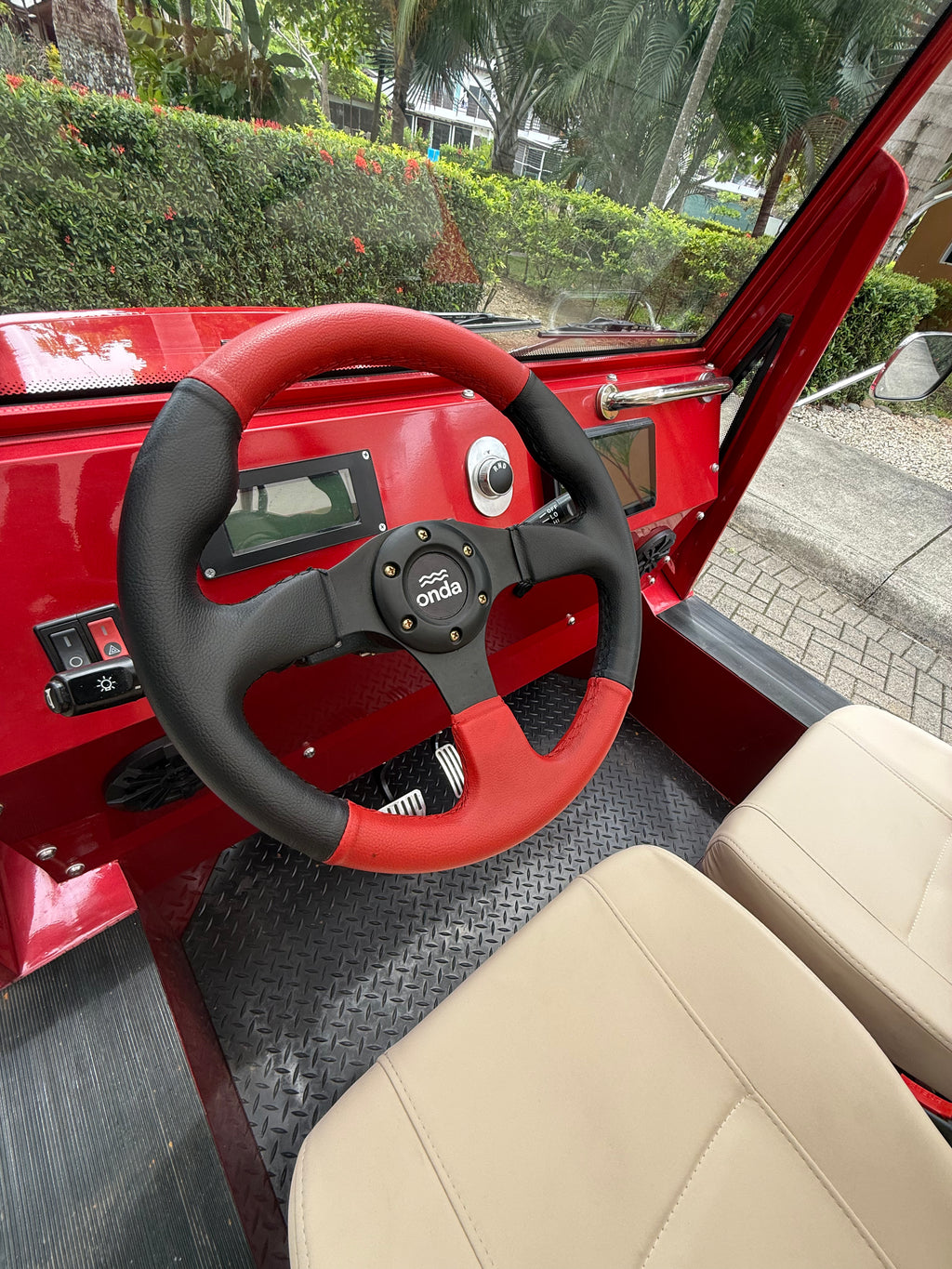 Red vehicle interior with a black steering wheel and beige seats.